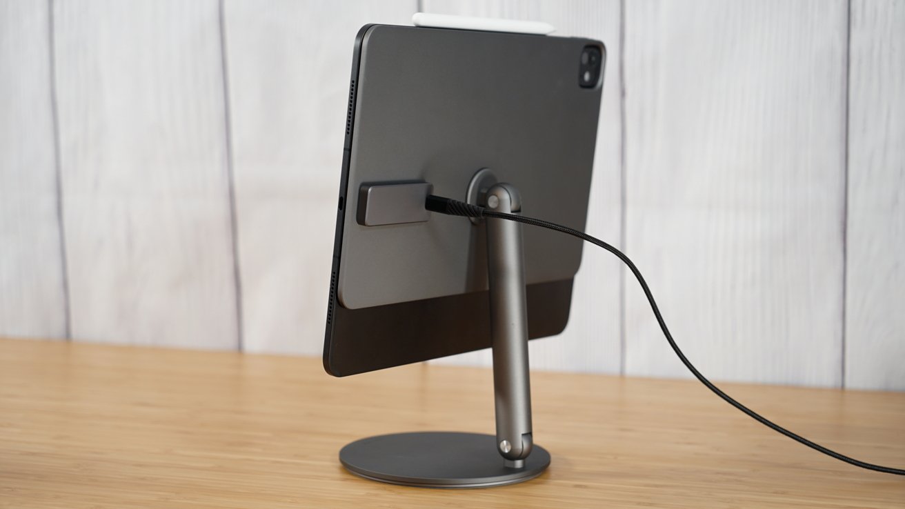 A black tablet on a stand, connected with a cable, sits on a wooden surface against a light background.