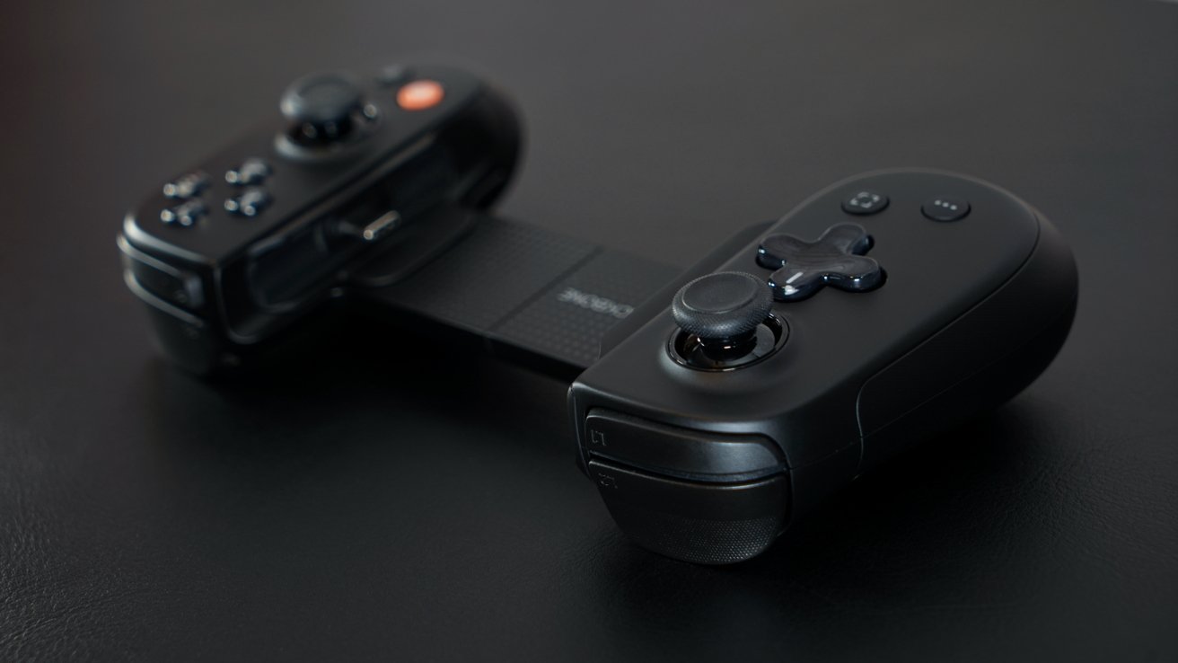 A black game controller with dual joysticks and buttons connected by a central textured strap, resting on a dark surface.
