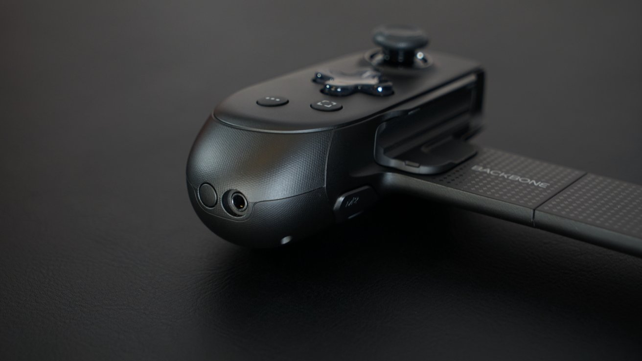 Black gaming controller on a dark surface, featuring buttons, joysticks, and connector.