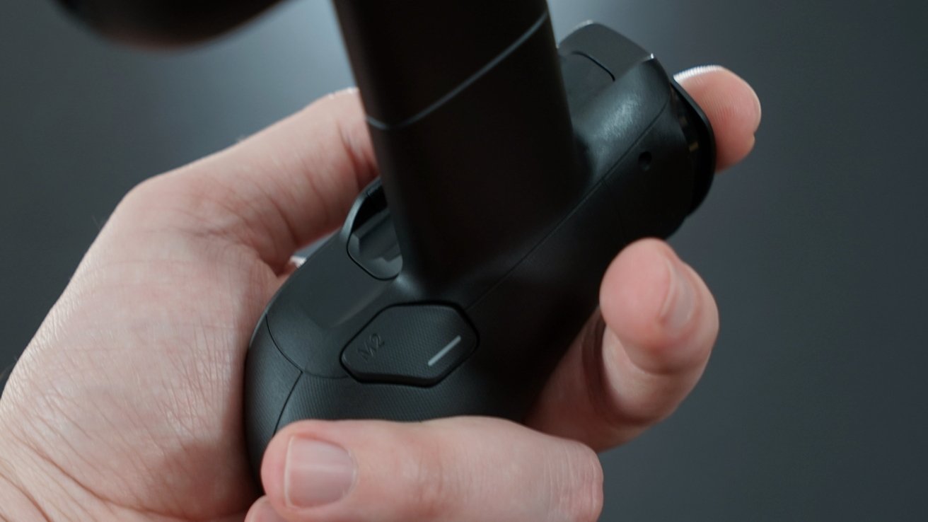 Hand gripping a black gaming controller, focusing on a button labeled 'M2,' against a blurred dark background.