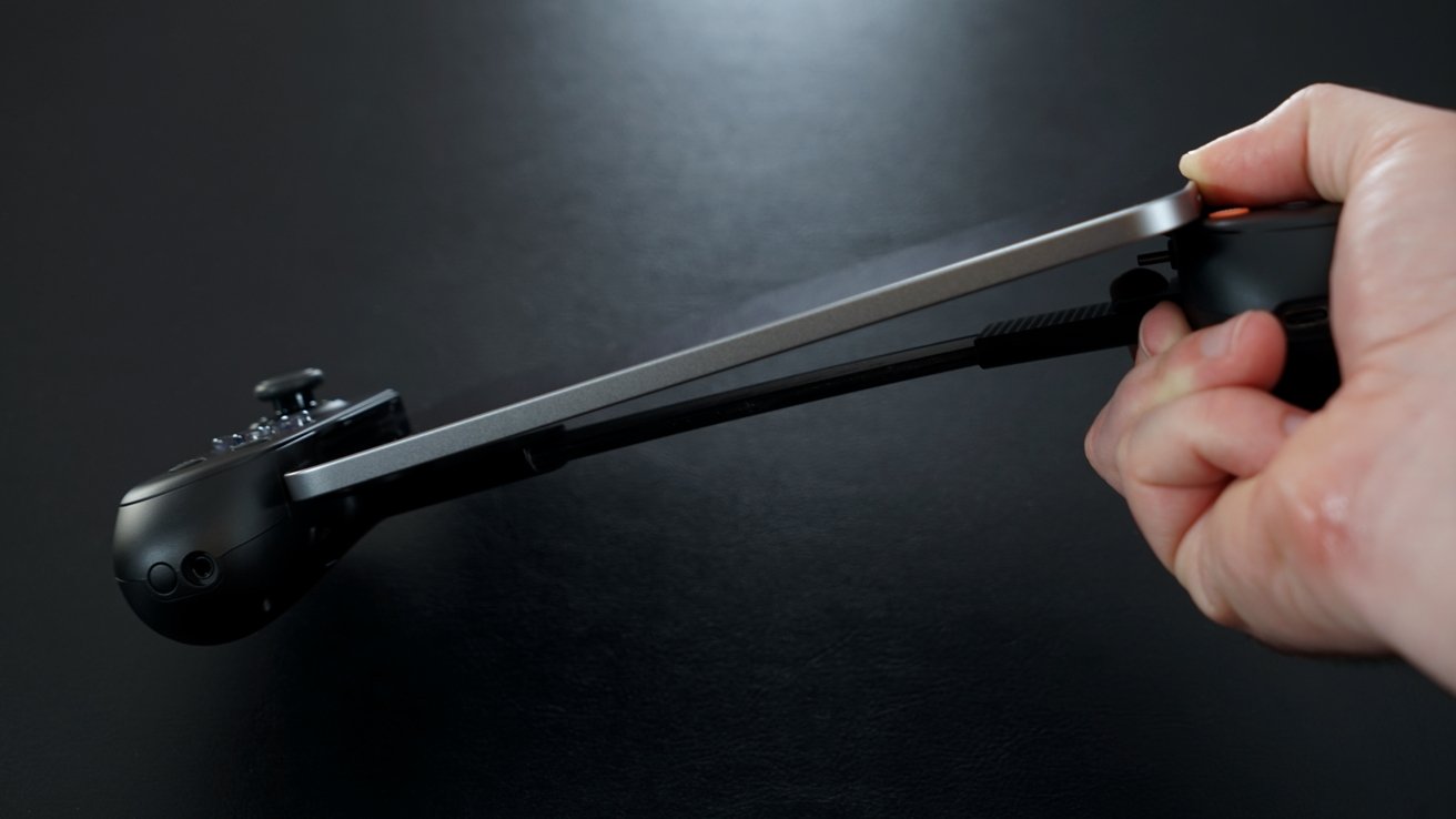 Hand holding a small handheld gaming device with a black joystick and buttons against a dark background.
